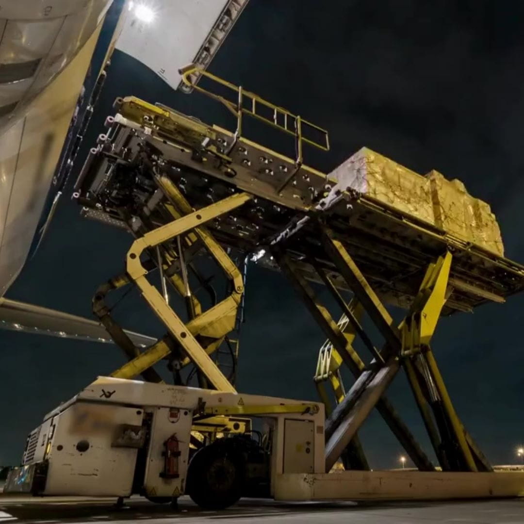 Freighter aircraft being loaded with palletized cargo at night on an airport apron.